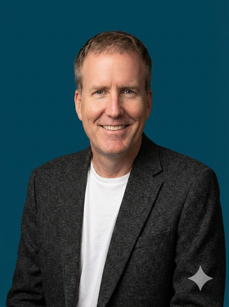 A photo of Larry wearing a black blazer over a white shirt with a dark blue background behind him.