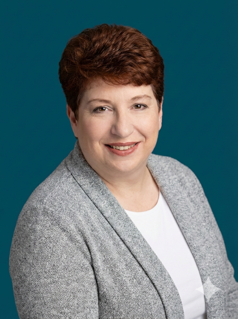 Photo shows Laura, a white woman with dark red hair and brown eyes. She has on a gray sweater over a white blouse against a dark blue background.