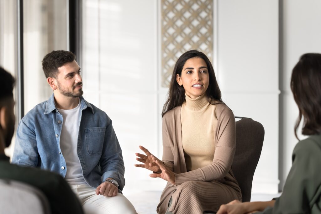 Photo of a group of four individuals having a discussion. A man and woman are centered in the photo with the woman gesturing and holding the conversation focus.