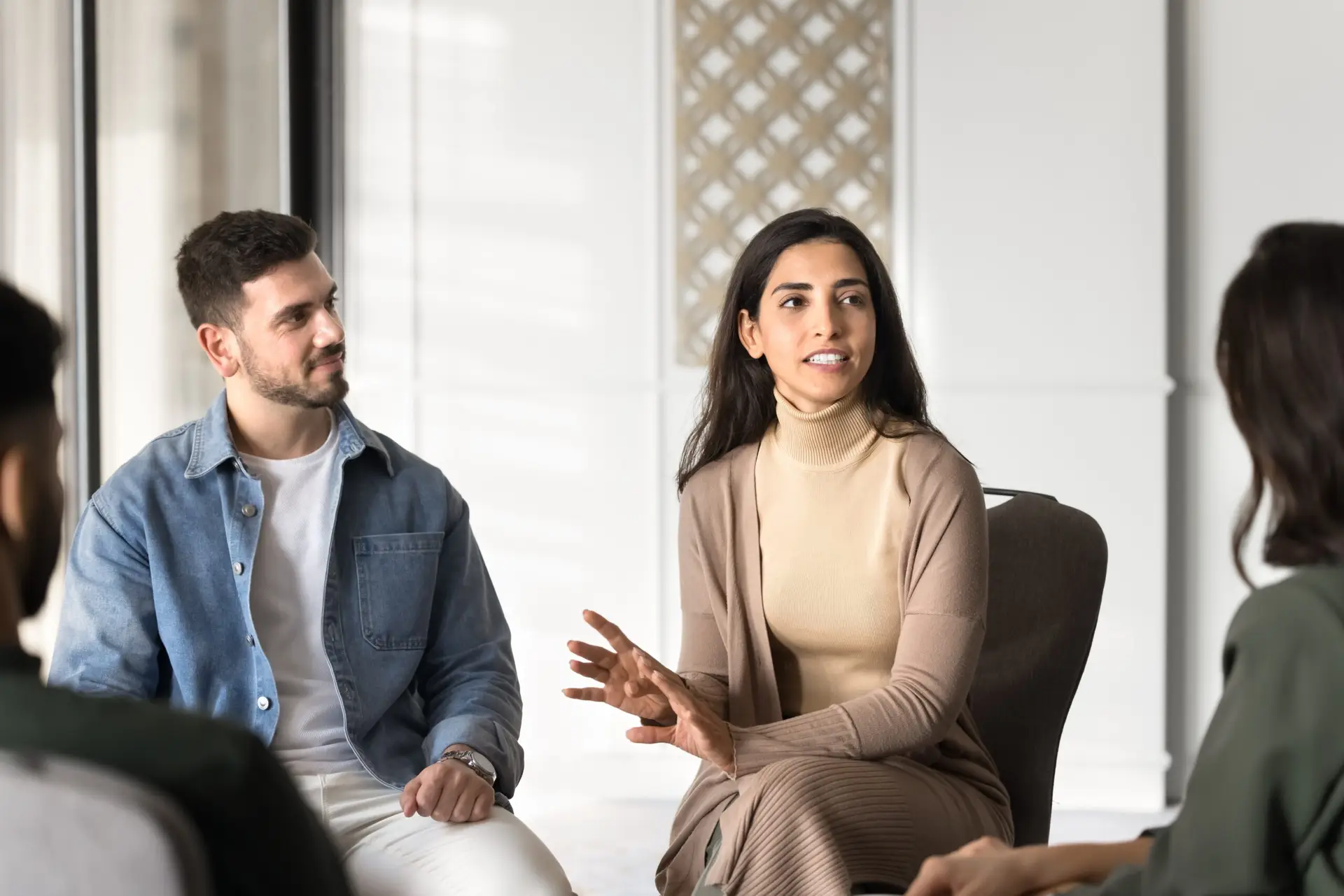Photo of a group of four individuals having a discussion. A man and woman are centered in the photo with the  woman gesturing and holding the conversation focus.